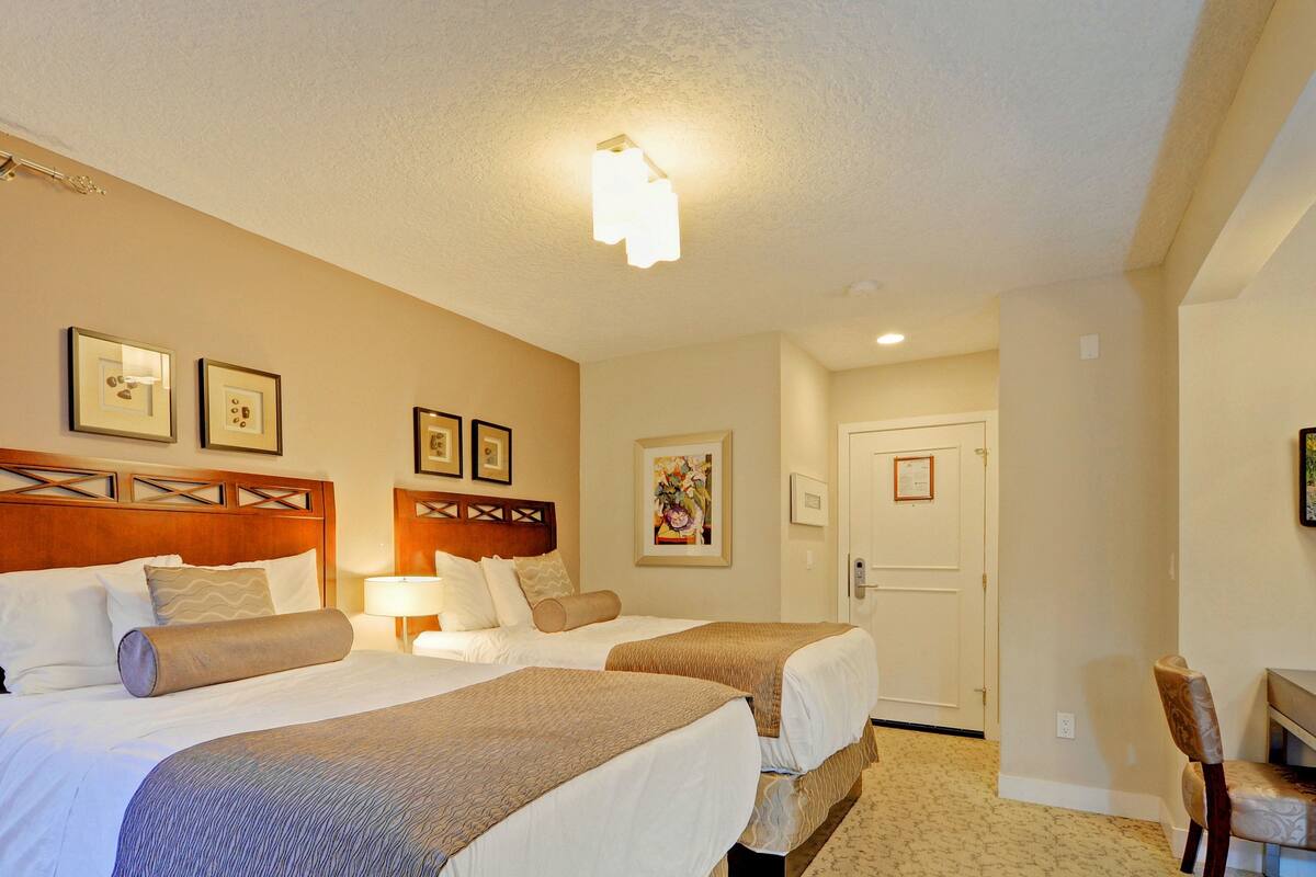A hotel room with two beds, a desk, and a chair.