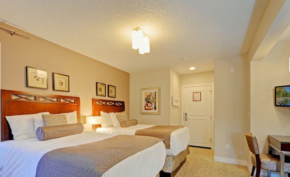 A hotel room with two beds, a desk, and a chair. - Helms Inn (Victoria)
