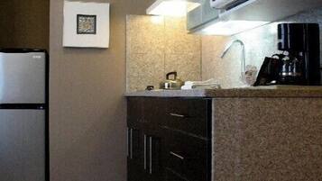 A compact kitchen with a refrigerator, microwave, and a coffee maker on the counter. There are two framed pictures on the wall and a textured backsplash.