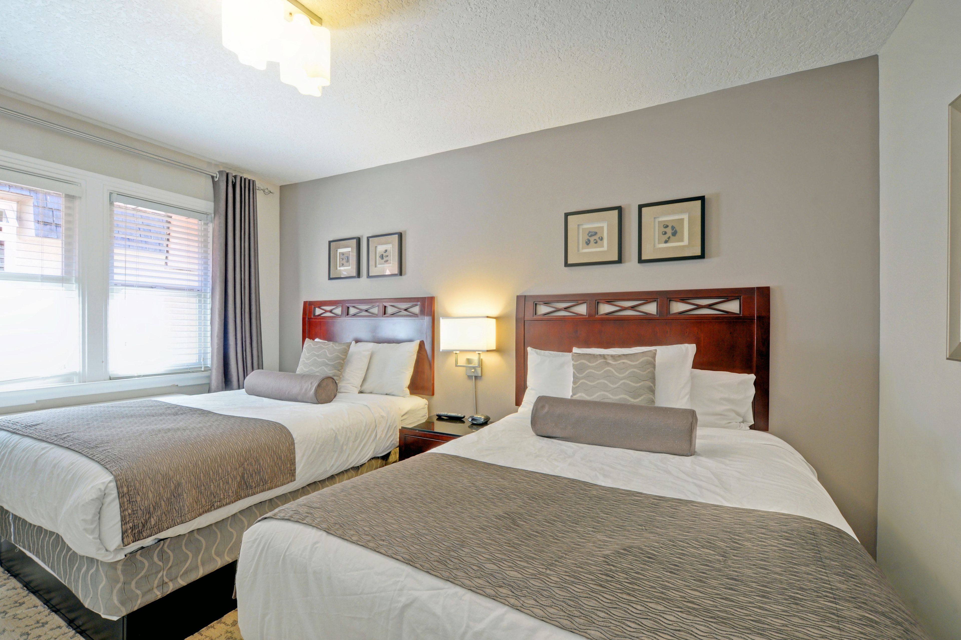 A hotel room with two beds, a nightstand with a lamp, and framed pictures on the wall.