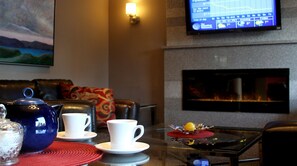 Un salon avec une cheminée, un téléviseur fixé au mur et une table basse avec des tasses et une théière.