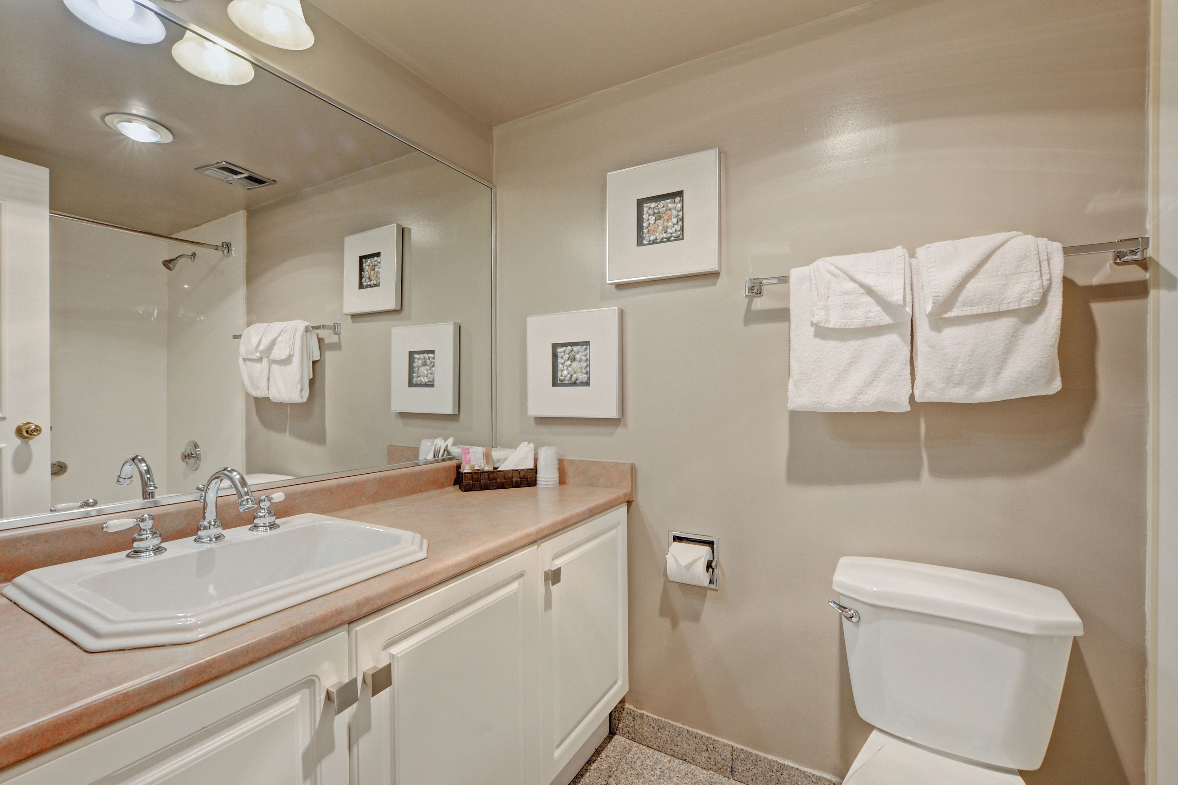 A bathroom with a sink, mirror, towel rack, toilet, and framed pictures on the wall.