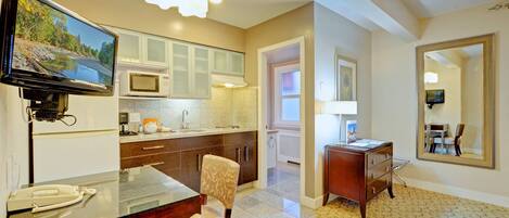 A modern kitchen with a flat-screen TV, white cabinets, a microwave, and a dining area with a chair and table.