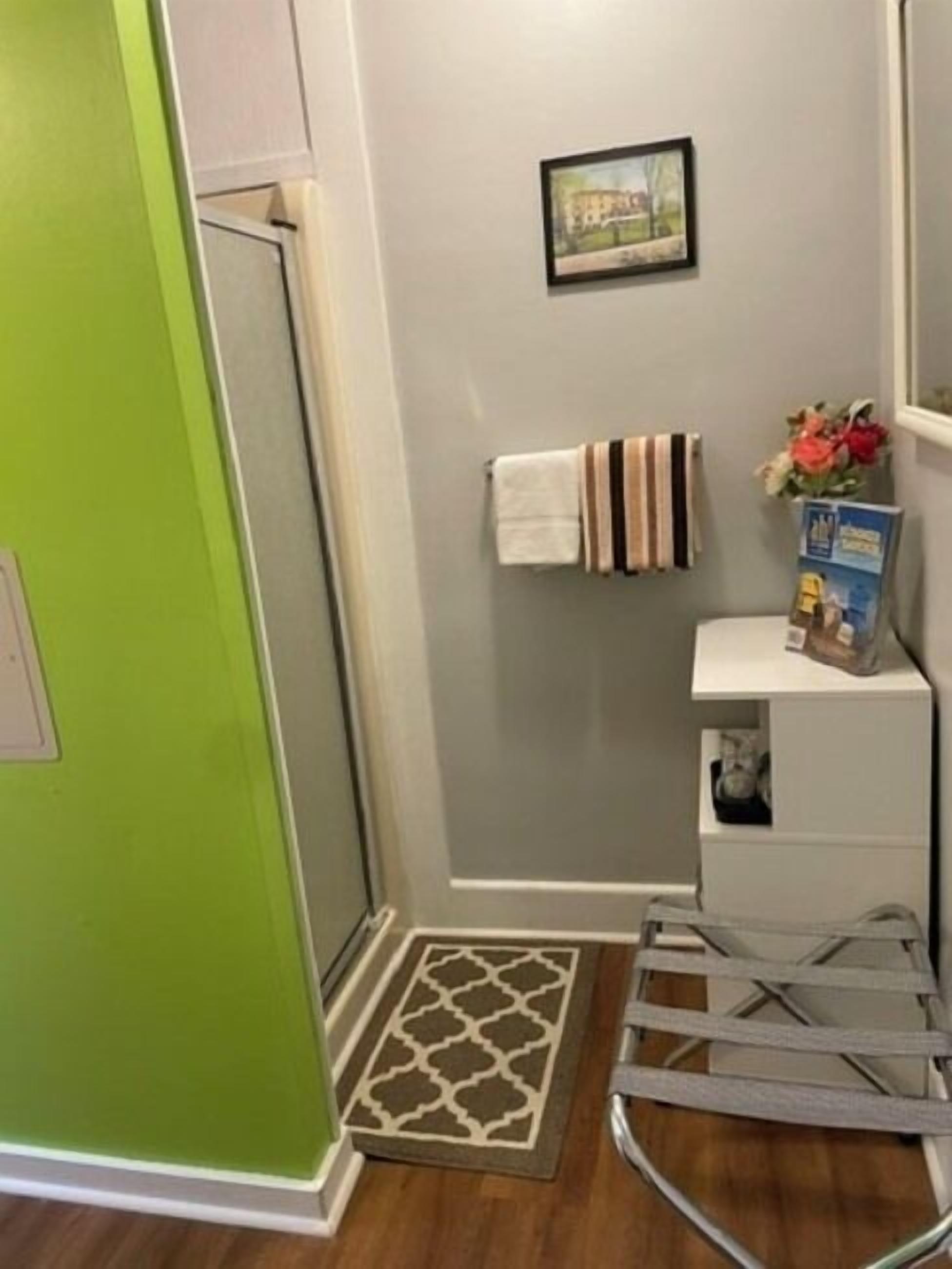 Ett badrum med en grön dörr, en handdukshängare med randiga handdukar, en inramad tavla på väggen och en liten hylla med en låda och blommor.