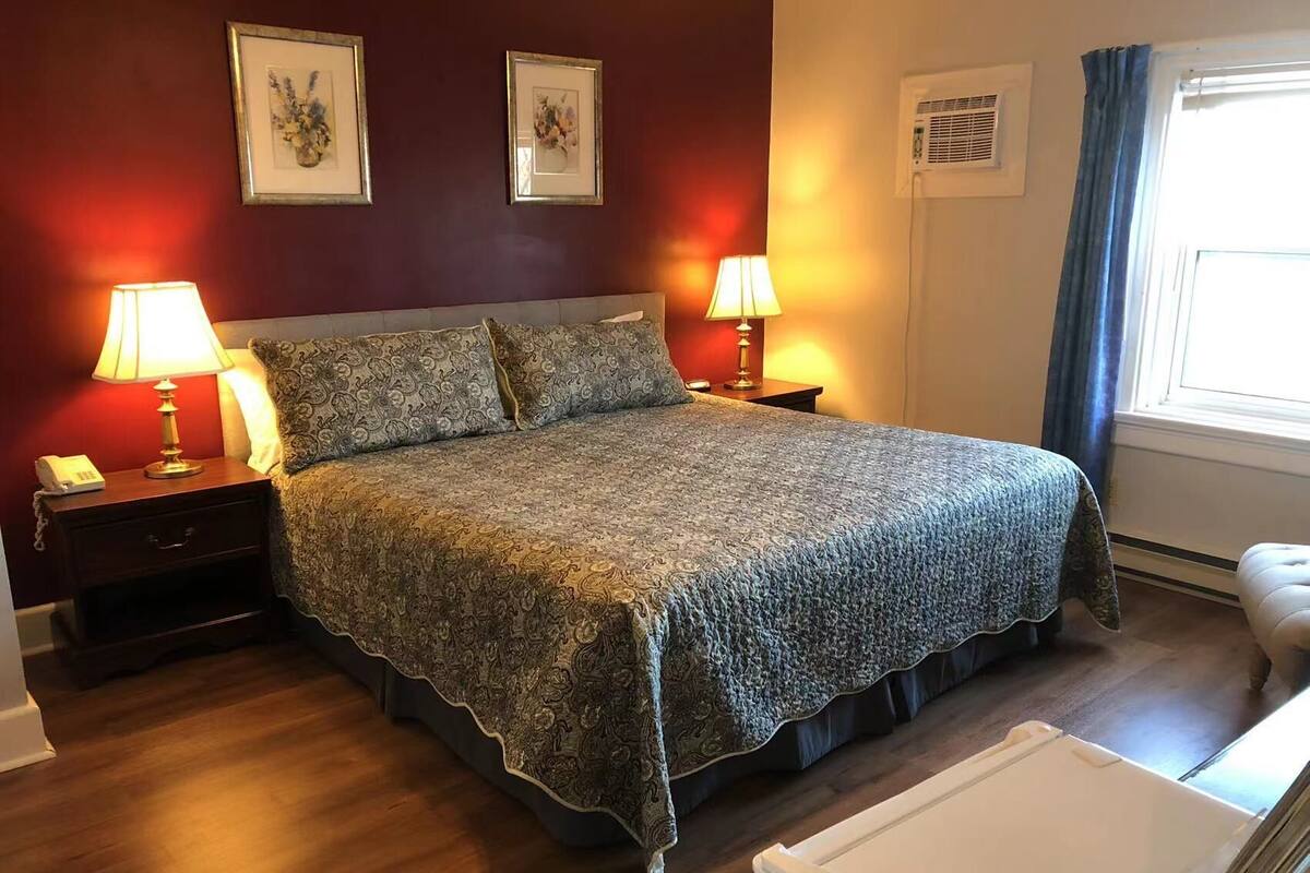 A neatly made bed with patterned bedding, two bedside lamps, a bedside telephone, and framed artwork on the wall.