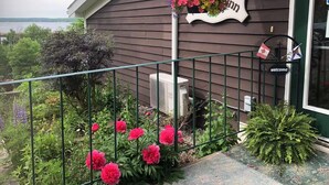 A house with a metal railing, a hanging flower basket, and a welcome sign with flags.