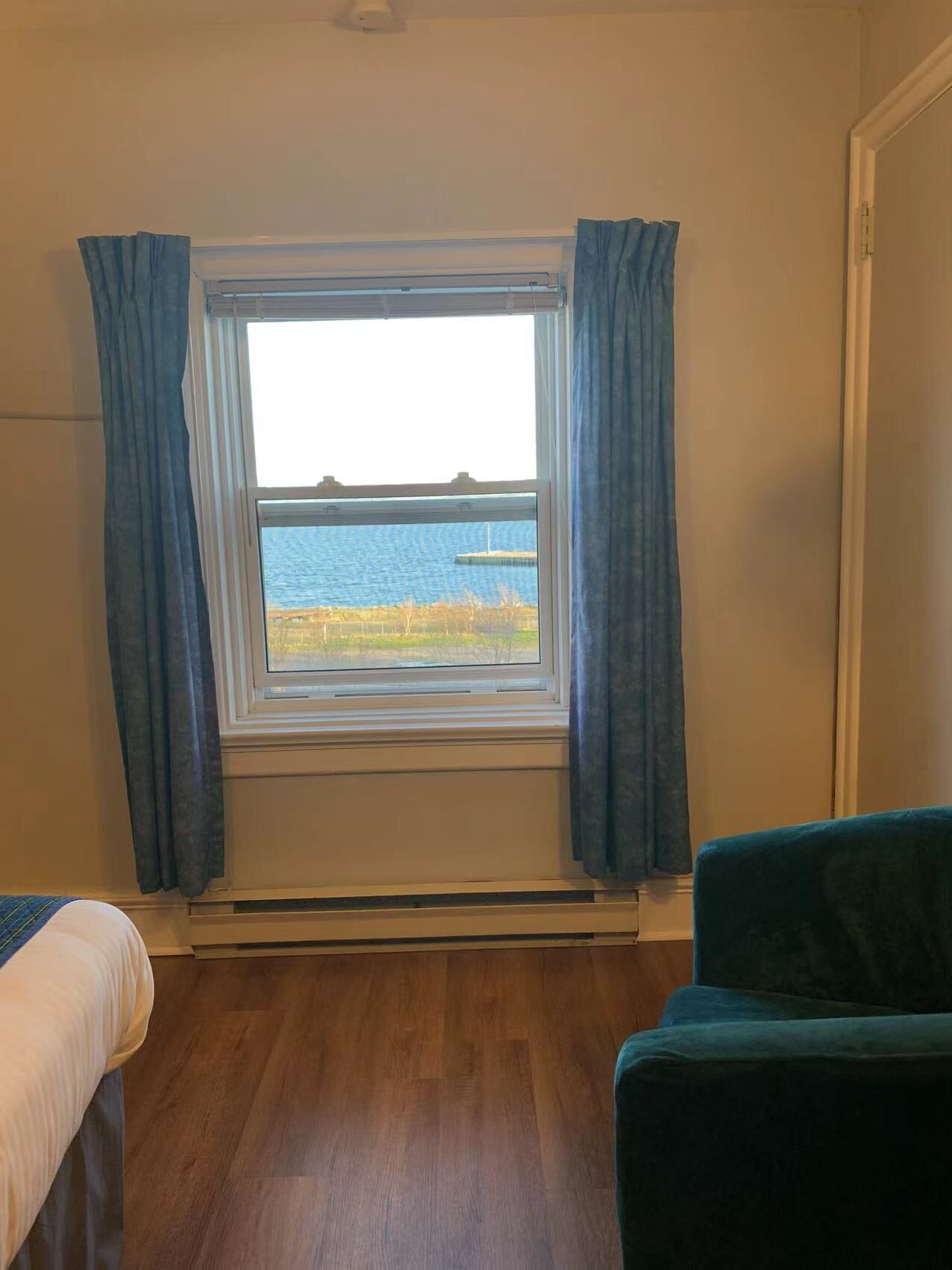 A room with a window overlooking a body of water, a bed, and a chair.