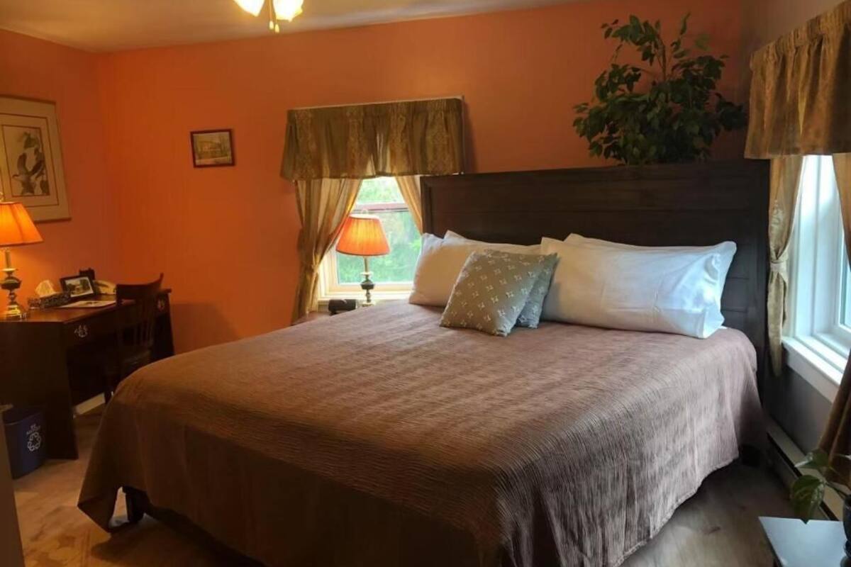 A bedroom with a large bed, a nightstand, a desk, and a window with curtains.