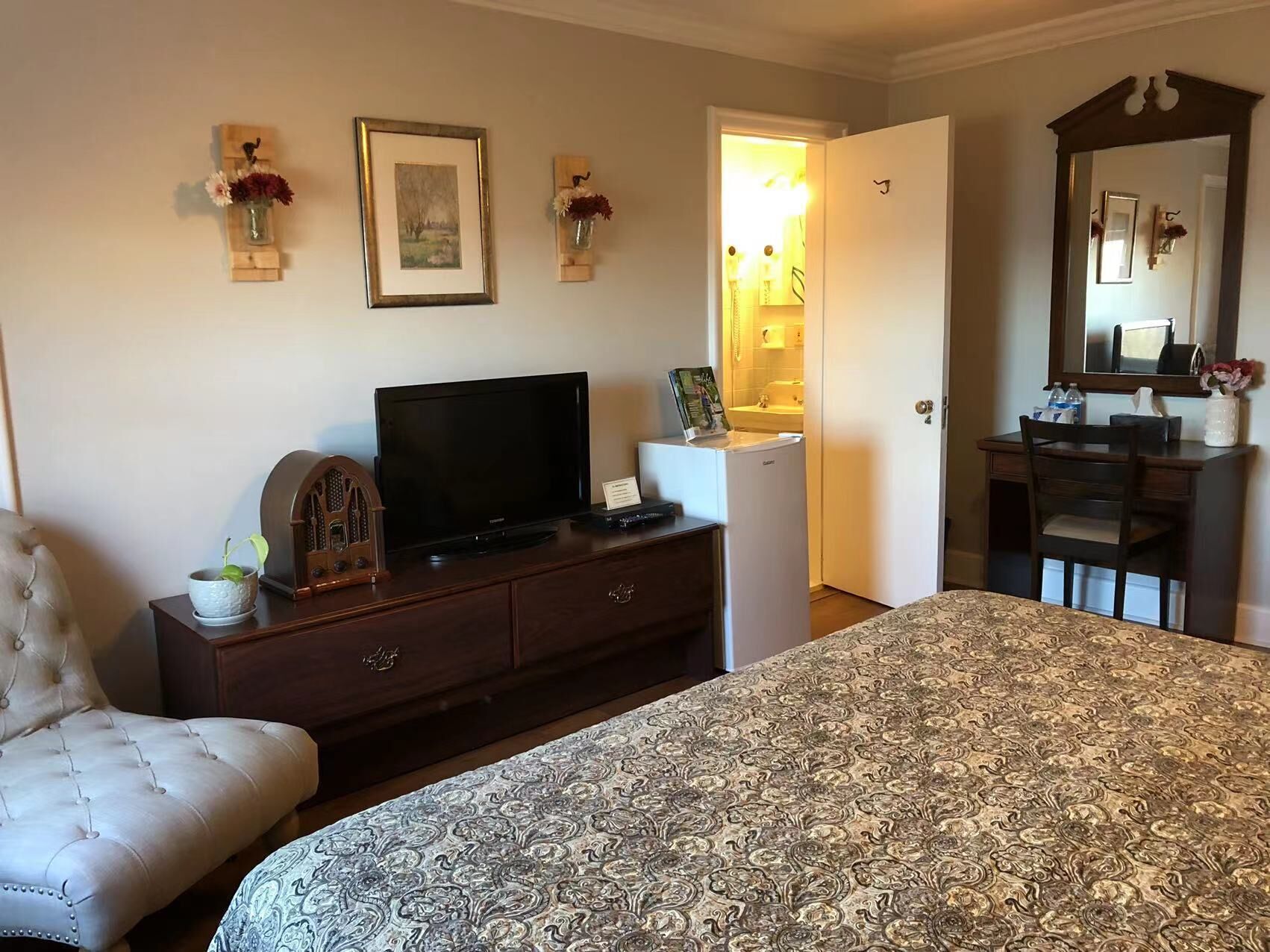 Una habitación de hotel con cama, televisor, cómoda, silla y escritorio con espejo.