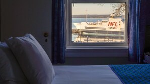 A hotel room with a bed, a window with a view of a ship labeled "NFL" docked at a pier.