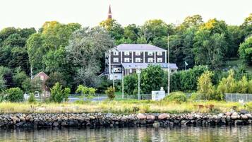 A large building with multiple windows and a flat roof, surrounded by trees and a body of water.
