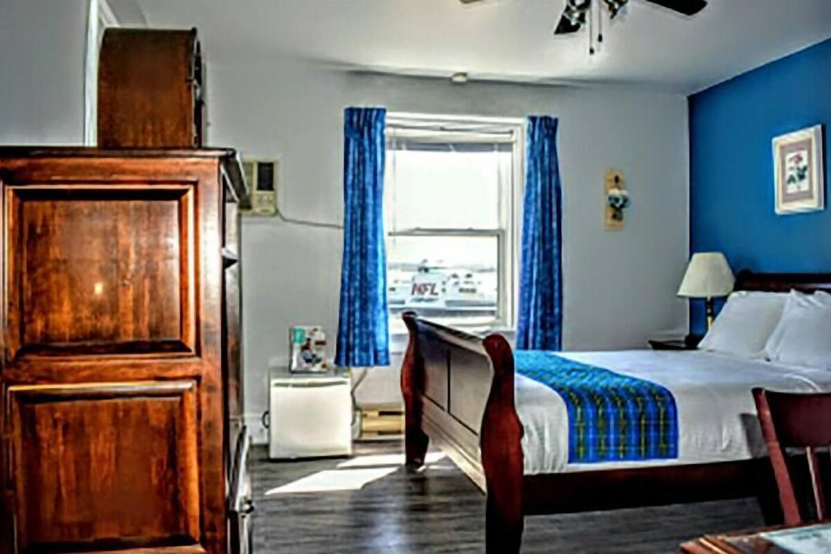 A bedroom with a wooden bed, a nightstand, a dresser, a window with curtains, and a wall-mounted lamp.