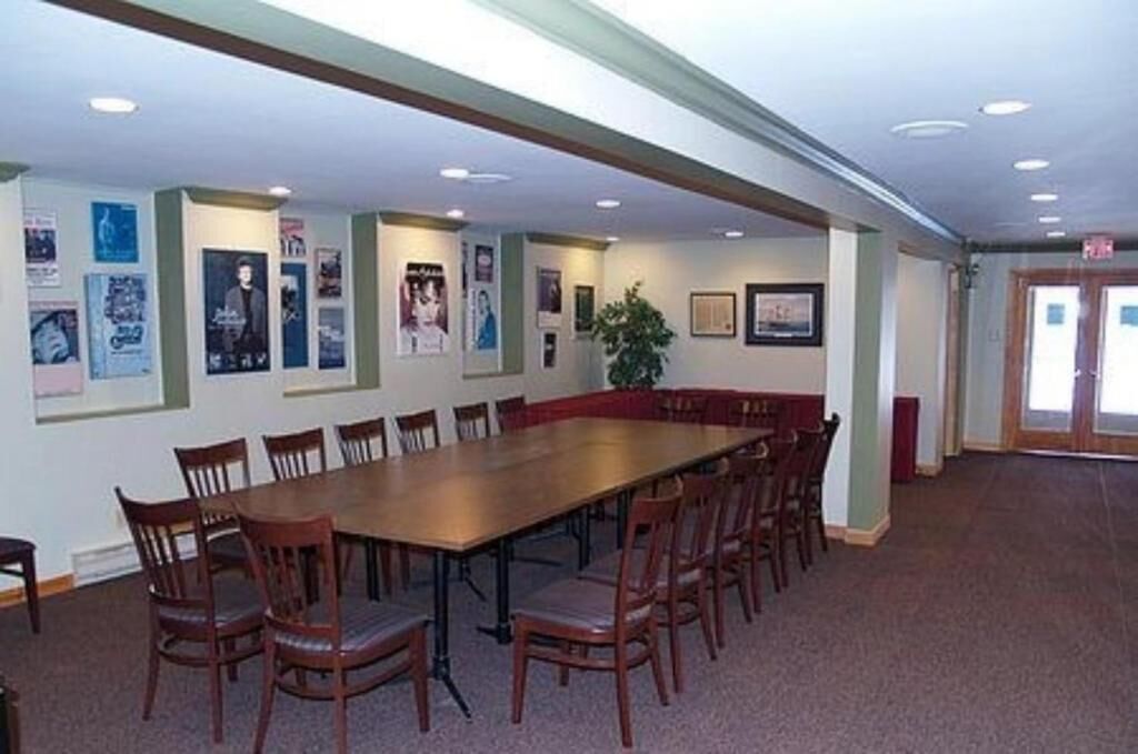 A conference room with a long table and chairs, posters on the walls, and a plant.