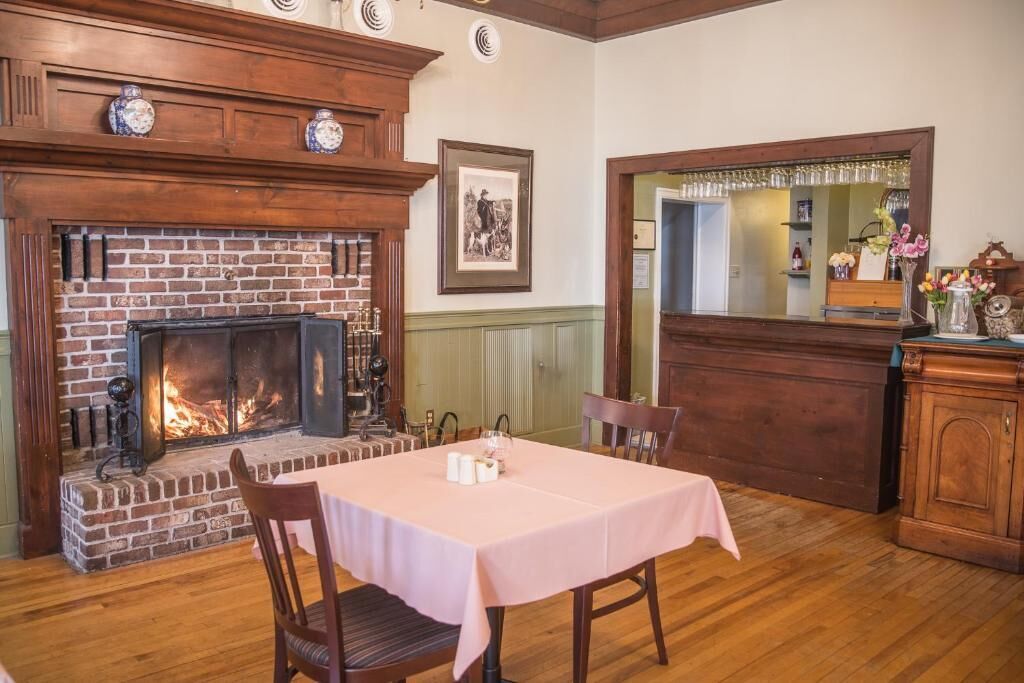A dining area with a brick fireplace, a table with a pink tablecloth, and wooden chairs.