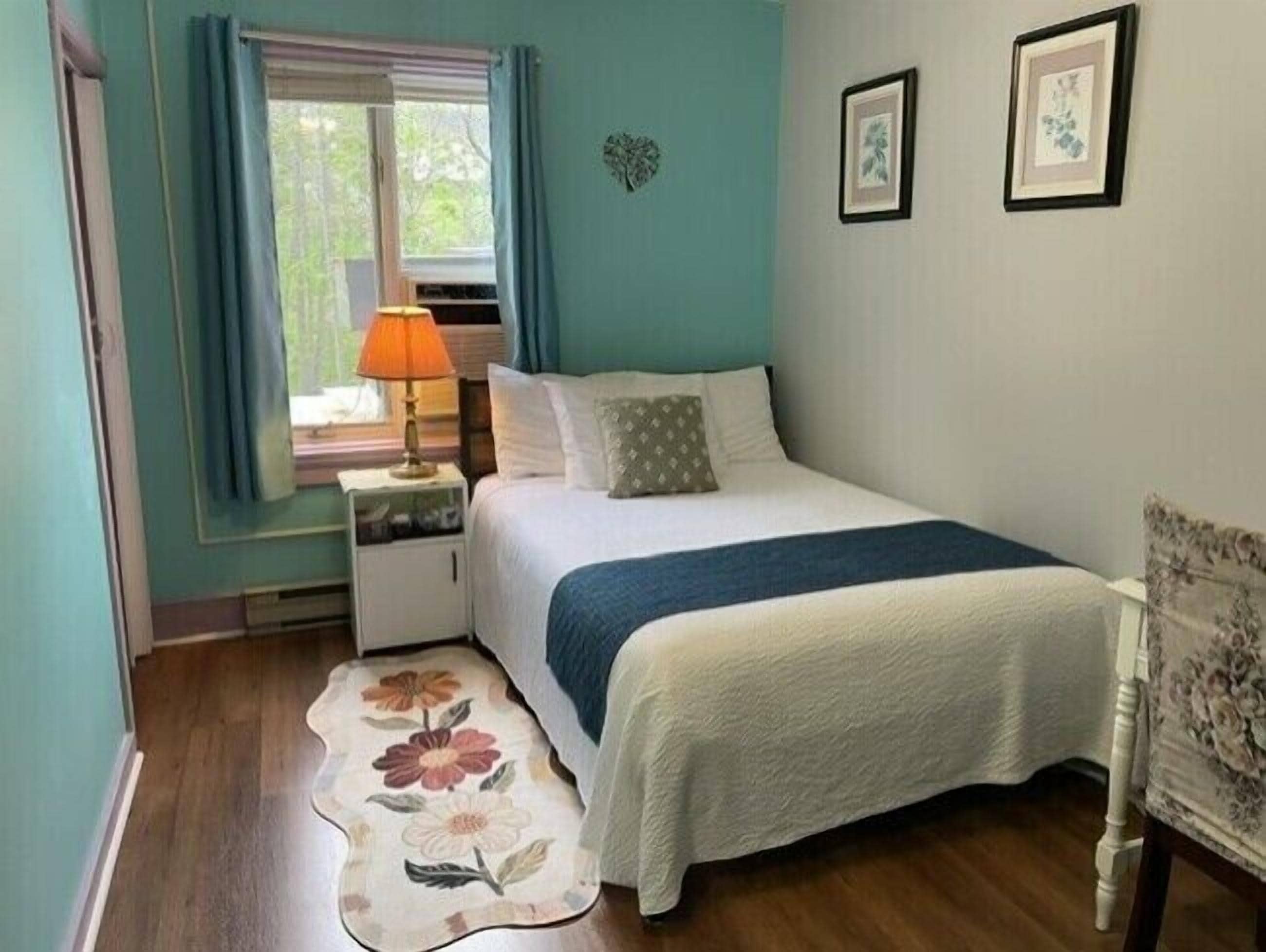 Une chambre à coucher comprenant un lit, une table de chevet, une lampe, un tapis à motifs floraux et deux tableaux encadrés accrochés au mur.