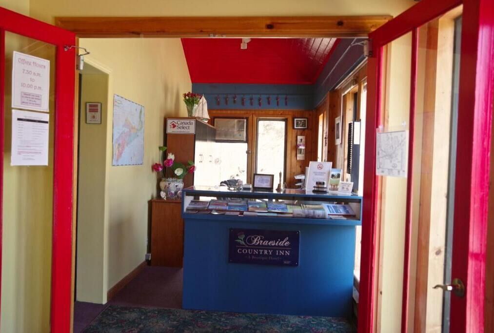 A hallway leading to a reception desk at Braeside Country Inn, featuring a red door, a wooden ceiling, and a map on the wall.