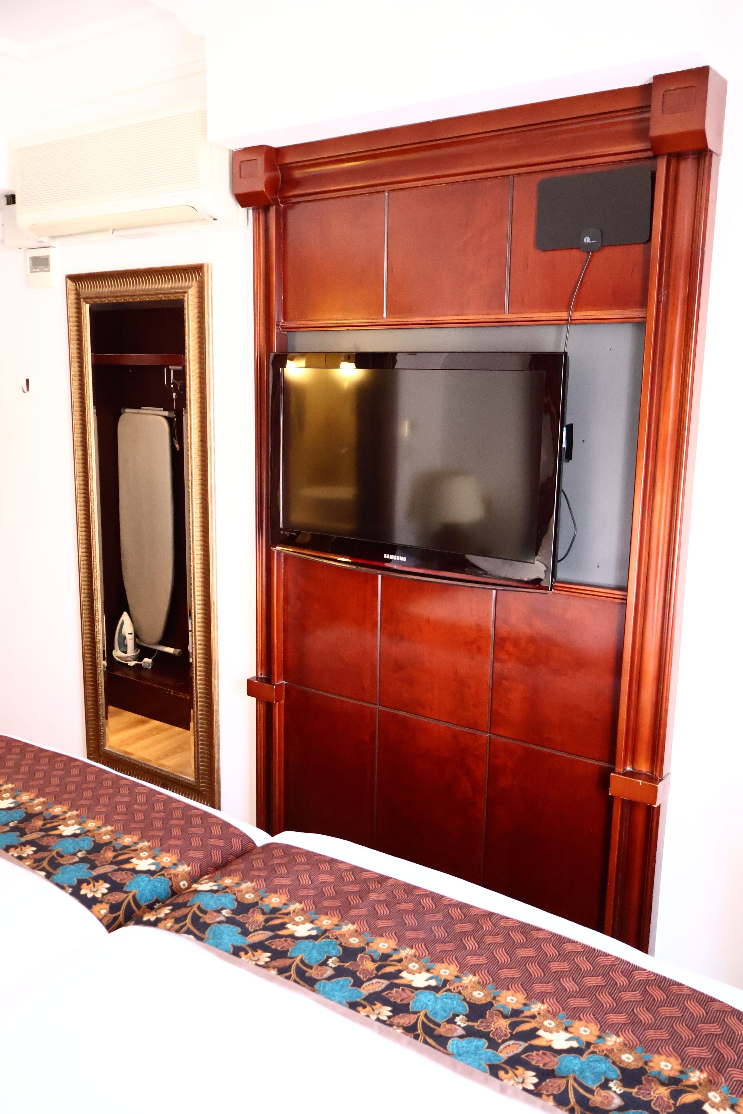 A room with a wooden panel wall, a flat-screen TV mounted above a mirror, and a patterned carpet.