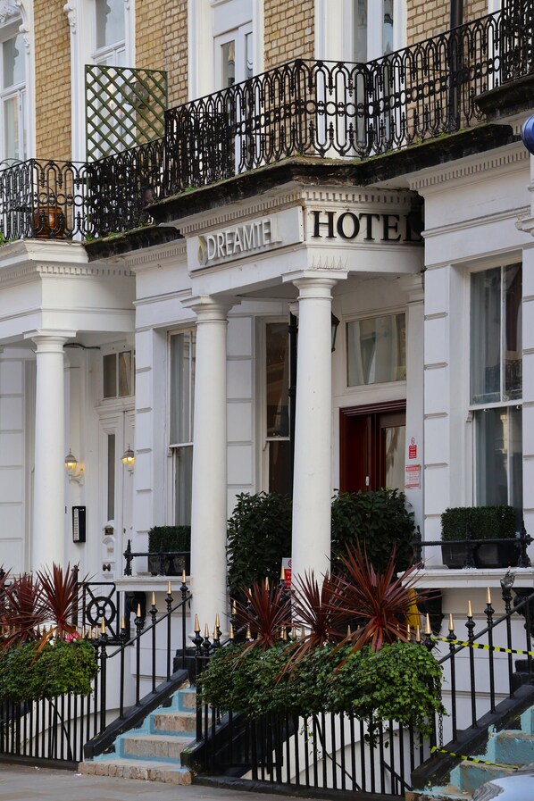 A white building with "DREAMIE HOTEL" signage, a black wrought iron balcony, and a staircase with blue steps. - Dreamtel London Kensington (London)