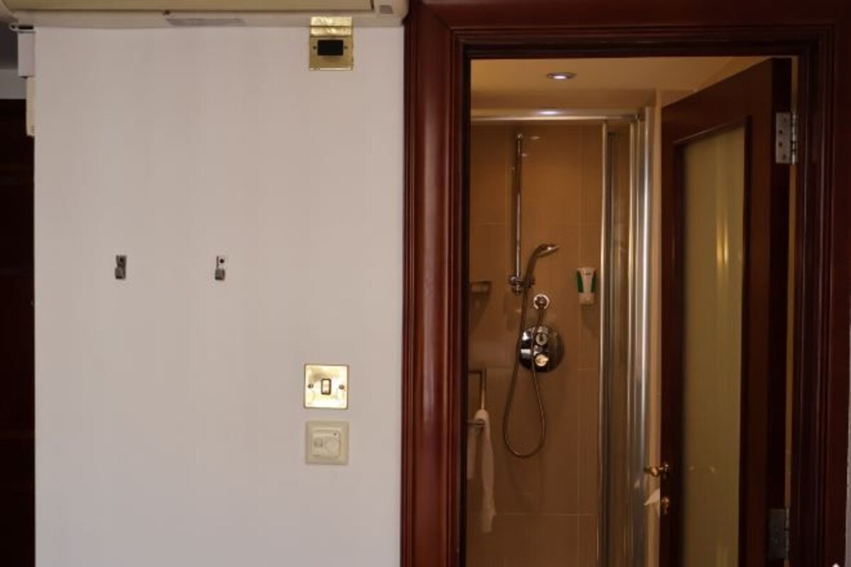 Quarto de hotel com área de chuveiro, uma porta e parede com dois interruptores de luz.