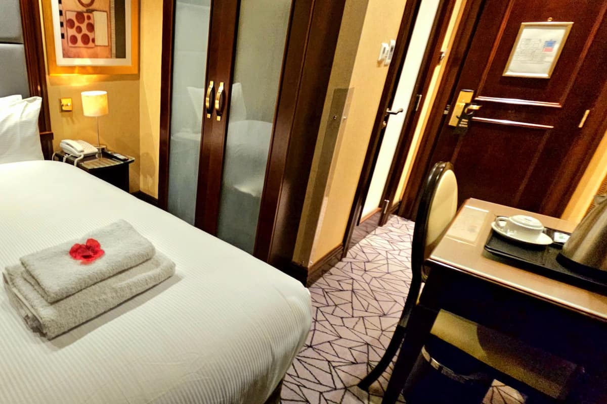 A hotel room with a bed, a bedside table with a phone, a mirror, and a door.