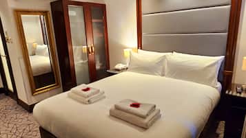 A hotel room with a large bed, a mirror, a wardrobe, and a bedside table with a lamp.