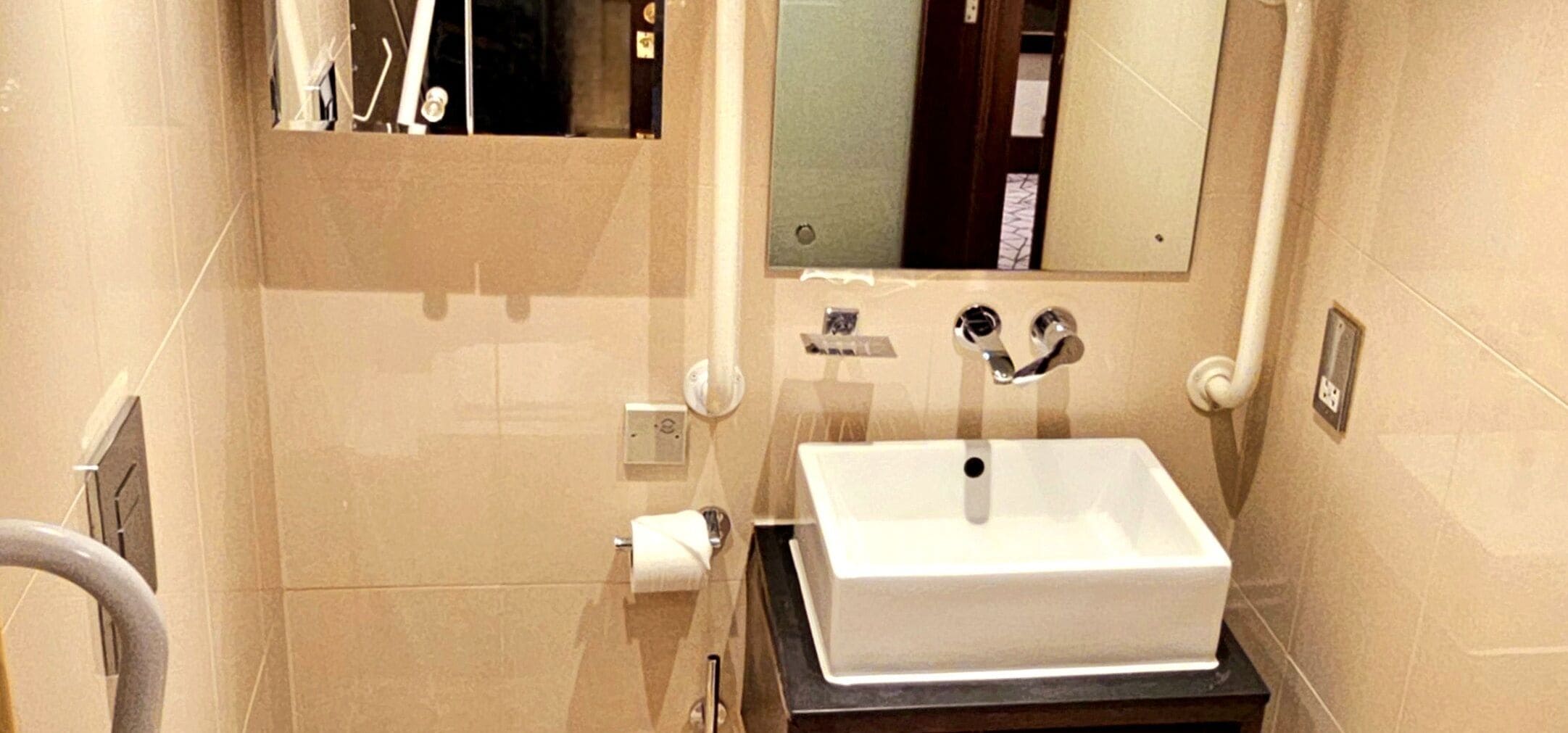 A bathroom with a white sink, a mirror, and a towel dispenser.