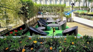 Un espacio al aire libre con mesas y sillas redondas, rodeado de follaje y flores.