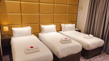 Three beds with white linens and pillows, a bedside table with a lamp, and a patterned tile floor.