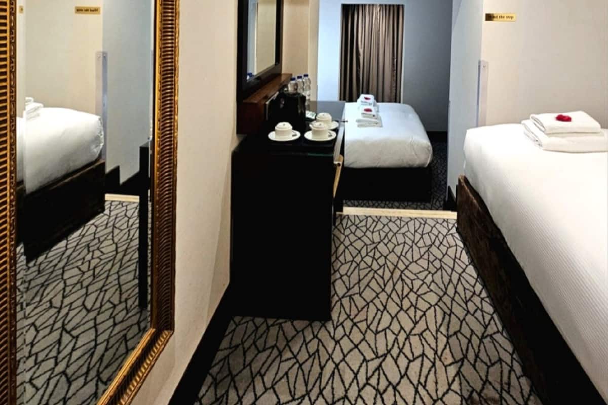 A hotel room with a large mirror, a bed, a desk with a chair, and a small table with a cup and saucer.