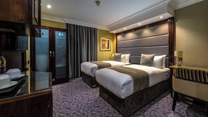 Habitación de hotel con una cama grande, dos mesitas de noche, un escritorio con silla, un espejo y una ventana con cortinas.