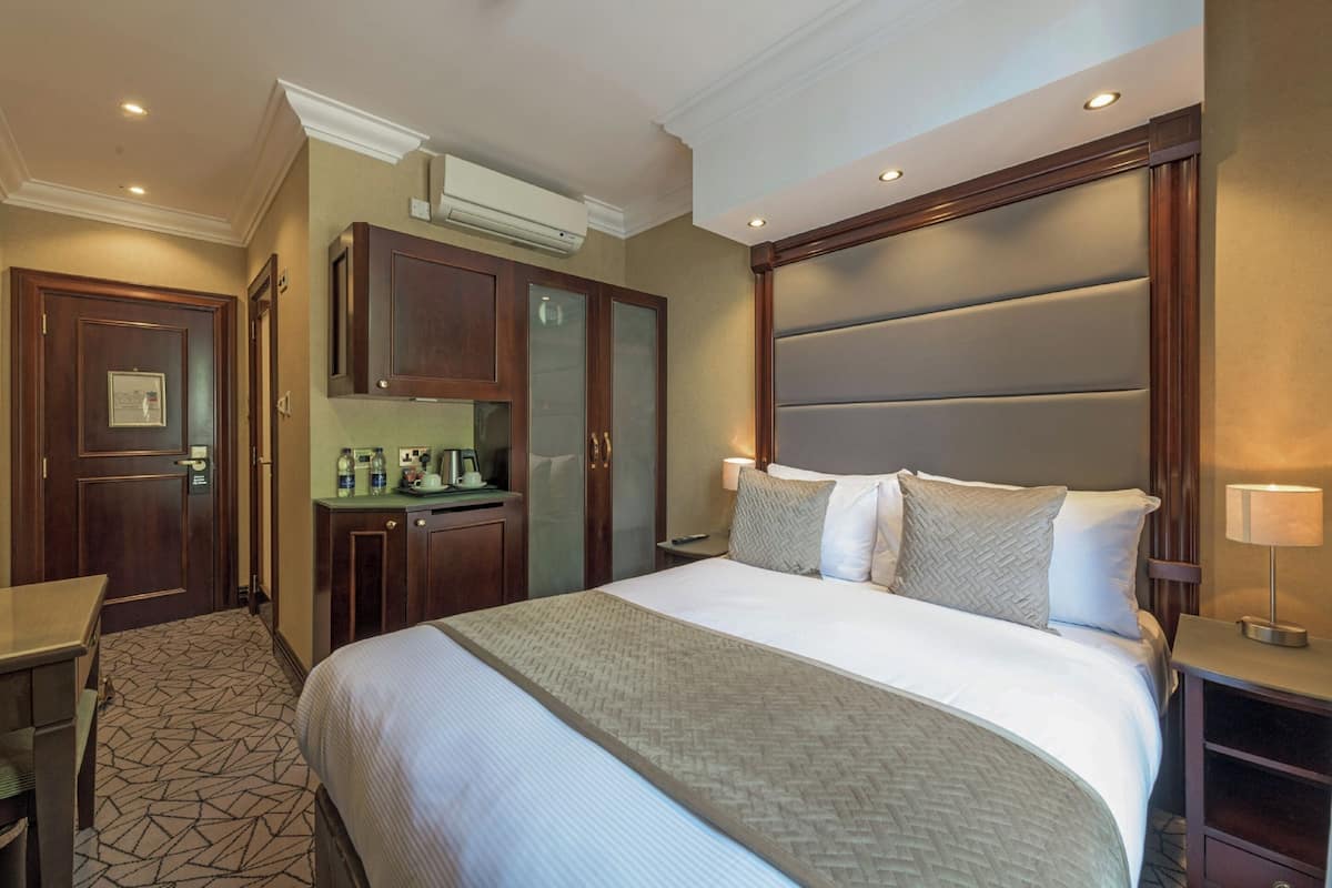 A hotel room with a large bed, a desk, a minibar, and a bathroom.