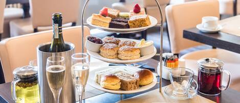A three-tiered dessert stand with various pastries and a bottle of champagne on a table in a restaurant.