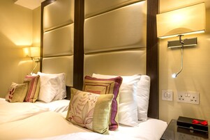 Ein Hotelzimmer mit einem großen Bett, mehreren Kissen, einem Nachttisch mit Lampe und einer Wandleuchte.