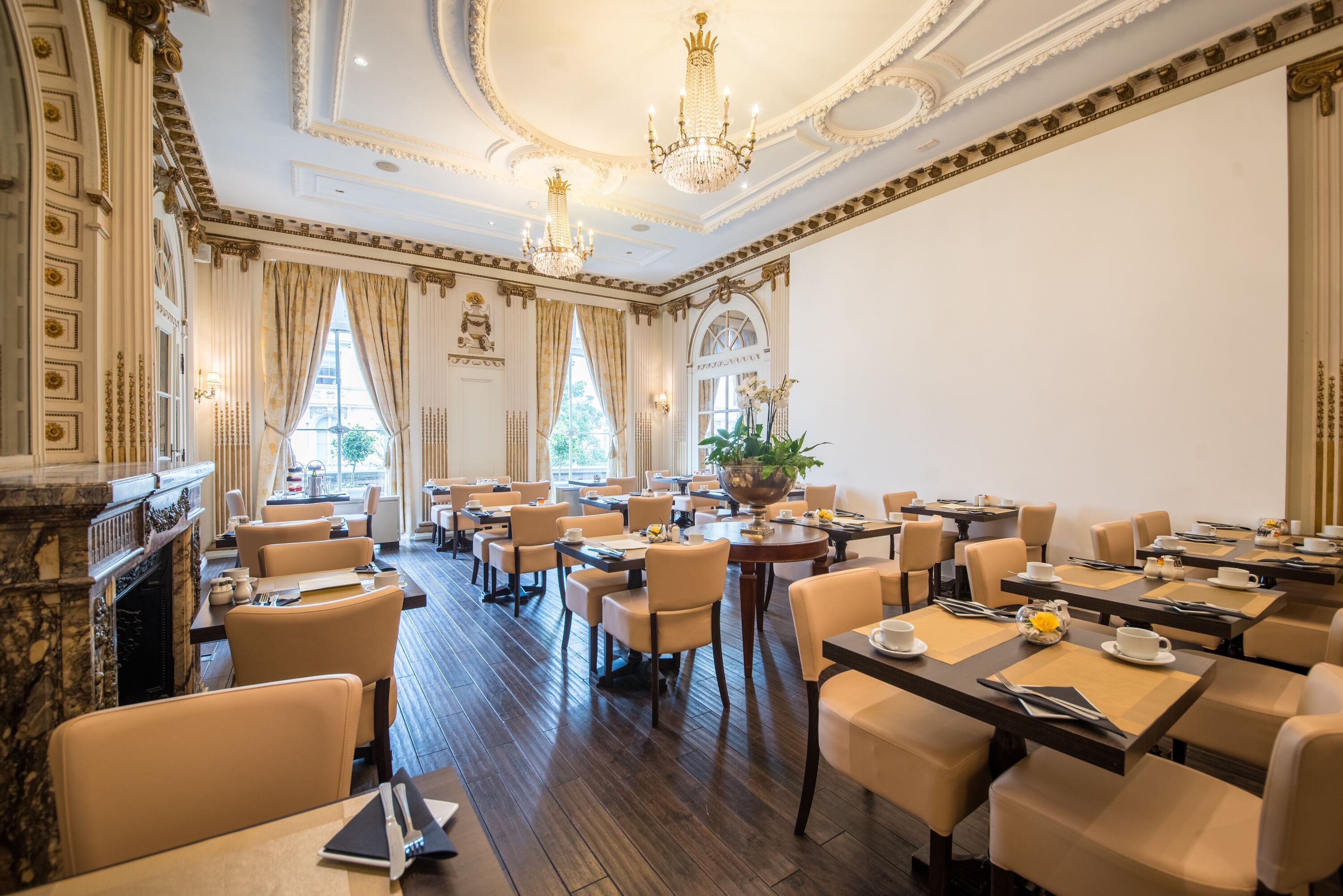Une salle à manger élégante, dotée de plusieurs tables et chaises, de lustres et d’une cheminée.