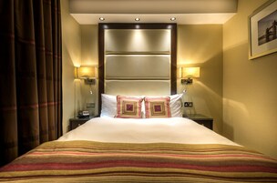 Ein Hotelzimmer mit einem großen Bett, zwei Nachttischlampen, einem Nachttisch und einem gerahmten Bild an der Wand.