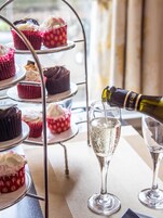Ein gestaffeltes Podest mit Cupcakes und einer Champagnerflasche, aus der in ein Glas eingeschenkt wird.