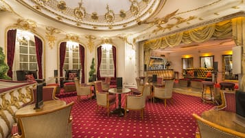 A luxurious room with ornate gold detailing, red velvet curtains, and a red carpeted floor.