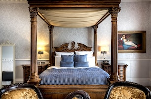 Ein Himmelsbett mit blauem Muster, zwei passende Kissen und ein Nachttisch mit Lampe.