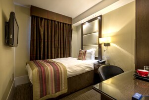 Ein Hotelzimmer mit einem Bett, einem Schreibtisch, einem Stuhl, einem Fernseher, einer Lampe und einer roten Schüssel auf dem Schreibtisch.