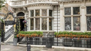 Un bâtiment historique doté d’une architecture riche en détails, d’une entrée imposante et d’un jardin bien entretenu où s’épanouissent de nombreuses plantes à fleurs.
