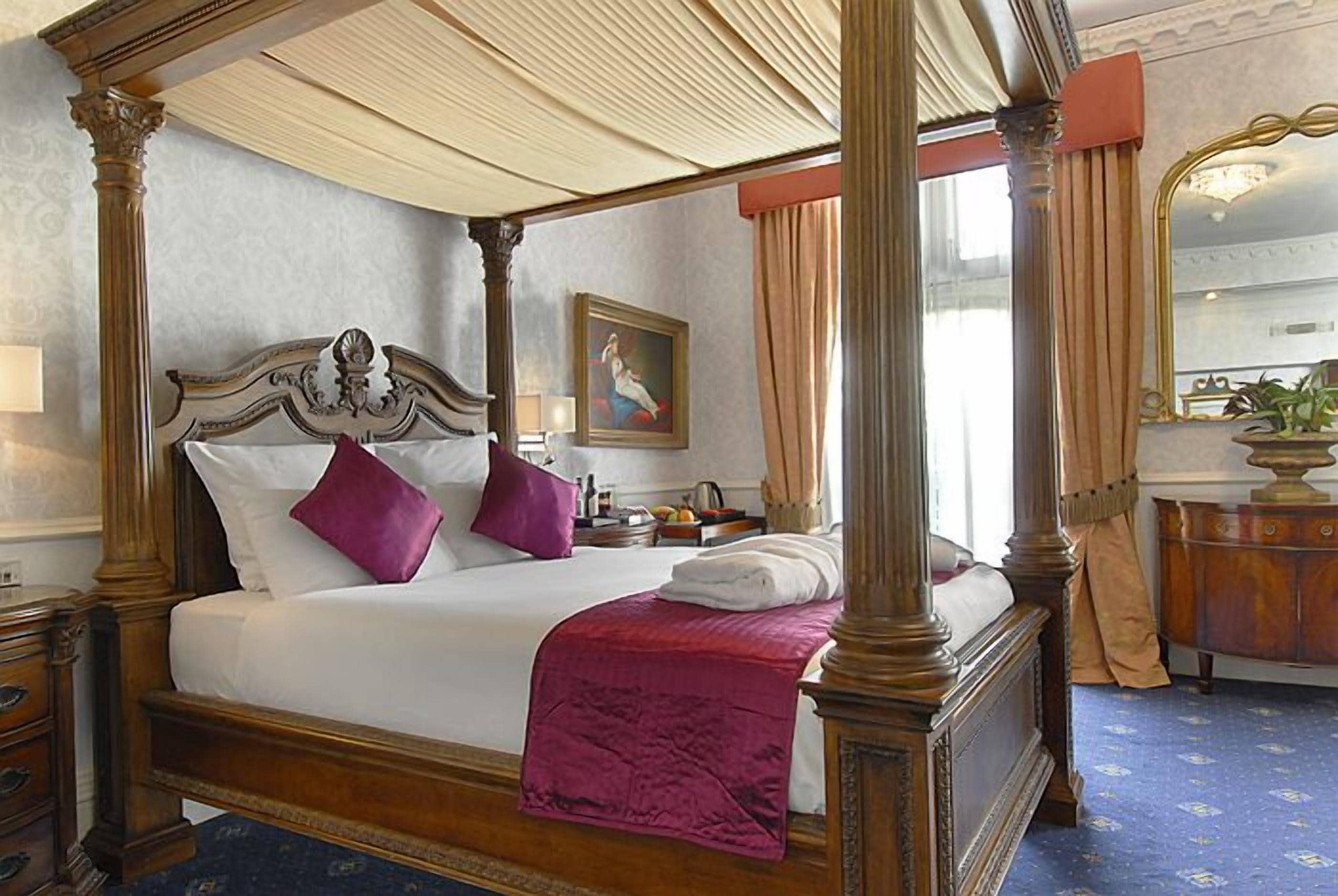 A four-poster bed with a canopy, a nightstand, a dresser, and a painting on the wall.
