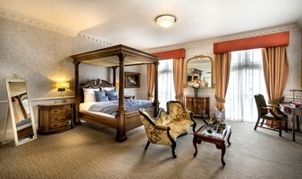 Ein Himmelbett mit Baldachin, ein bequemer Sessel, ein kleiner Tisch mit Blumenvase und ein Schreibtisch mit Lampe.