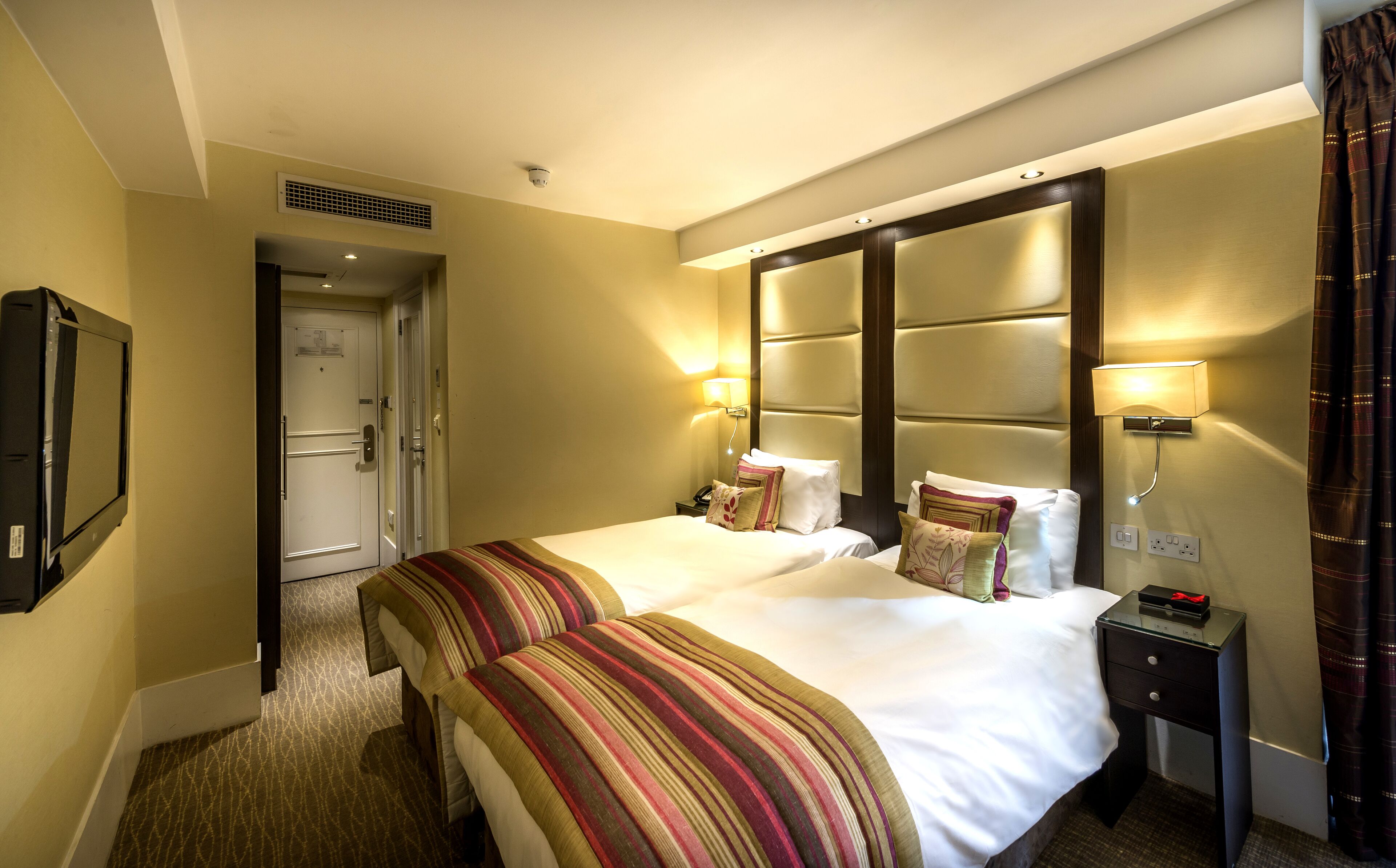Une chambre d’hôtel avec deux lits, un bureau, une chaise, une télévision et une porte.