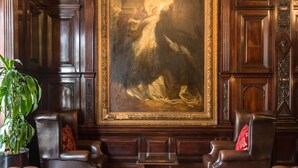 Une pièce avec un grand portrait, des fauteuils en cuir, une table basse sur laquelle est posée une carte, et une plante en pot.