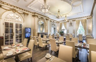 A luxurious dining room with ornate ceiling details, chandeliers, and a television screen.