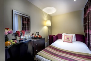 Ein Hotelzimmer mit Bett, Schreibtisch mit Lampe, Fenster mit Vorhängen und einer Blumenvase.
