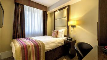 A hotel room with a bed, bedside table, lamp, and a desk with a chair.