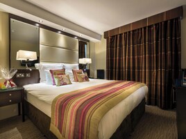 Ein Hotelzimmer mit einem großen Bett, zwei Nachttischlampen, einem Nachttisch, einem Spiegel und einem dunklen Vorhang.