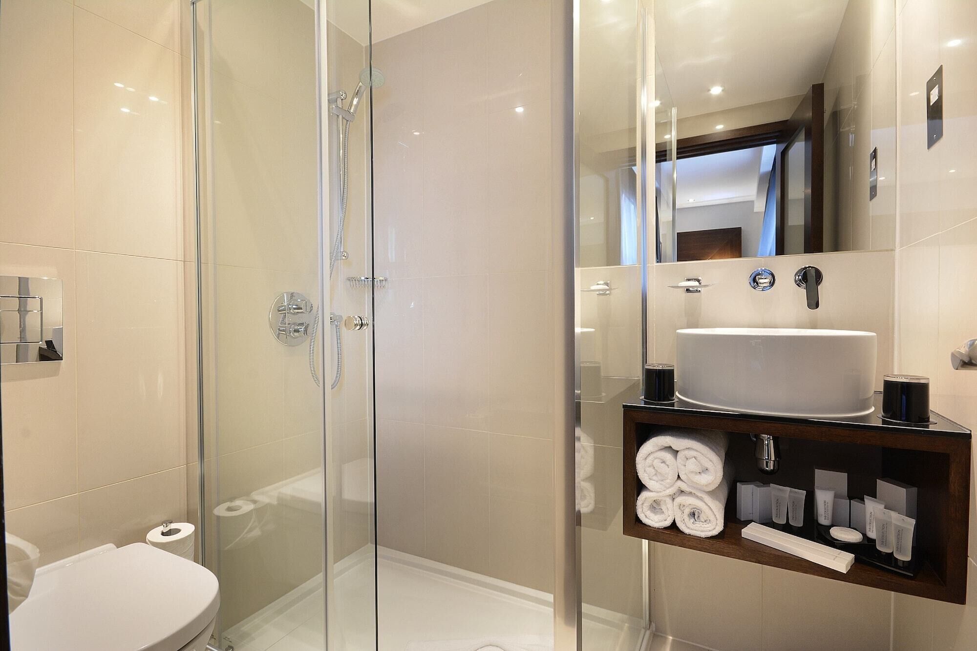 Une salle de bain moderne avec une douche à parois de verre, un lavabo blanc et un meuble-lavabo avec des articles de toilette.