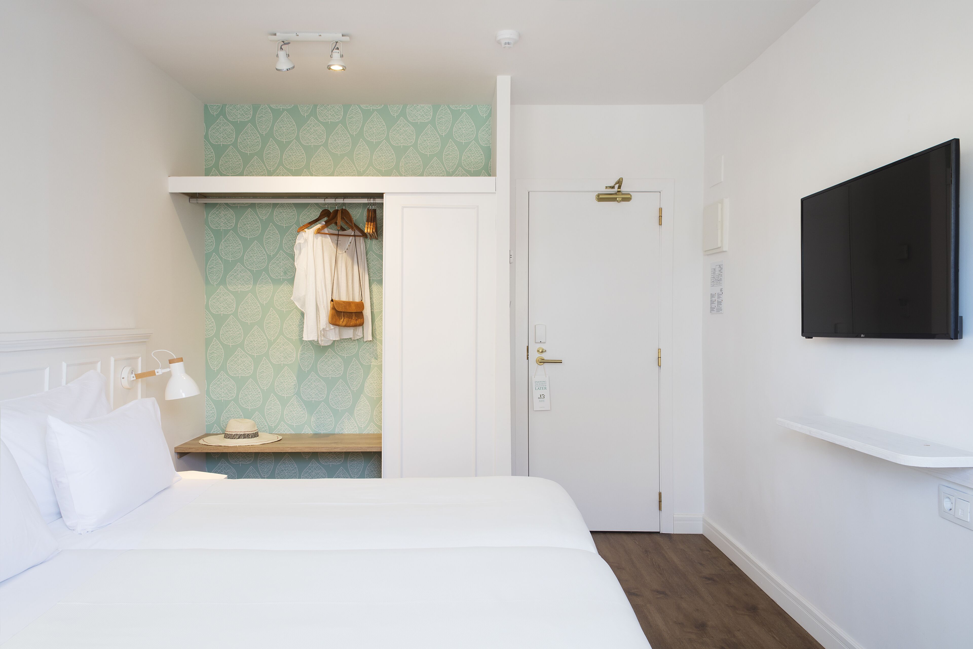 Una habitación de hotel con cama, armario, tocador con espejo y televisor montado en la pared.